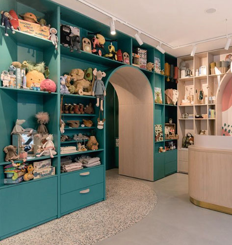 Photo de l'espace boutique. Espace d'étagères couleur turquoise et couleur bois, au centre une entrée vers une autre salle. Les étagères sont remplies de peluches et jouets colorés.