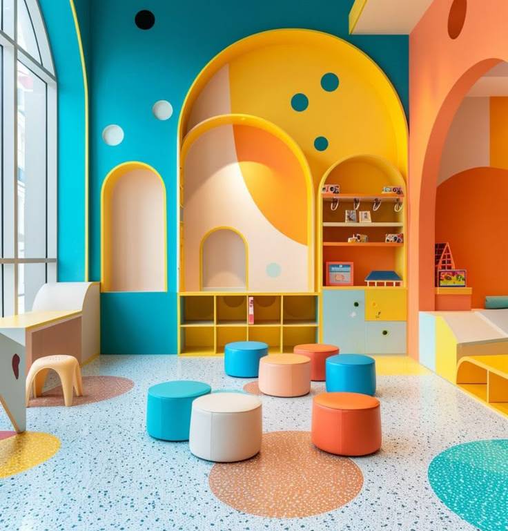 Espace Atelier, murs et déco très colorés, au sol des poufs et mobilier pour grimper dessus. Au fond des étagères avec le haut en arc arrondi. Couleur bleu ciel, jaune t orange.