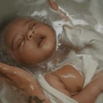 visuel Bain signature, bébé plongé dans un bain, des mains le soutienne