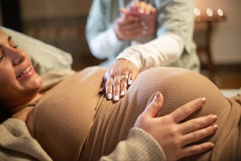 visuel Consultation prénatal, jeune femme enceinte, la médecin, a sa main sur le ventre de la femme.
