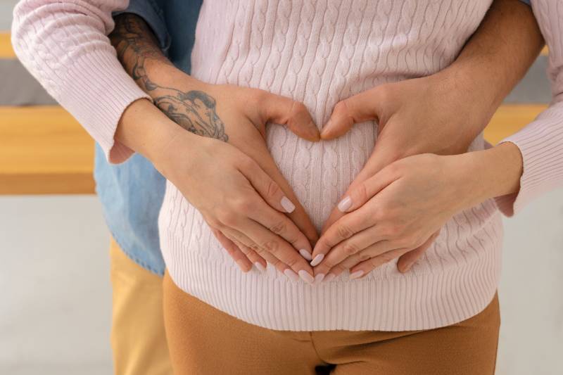 visuel Haptonomie, détail, couple, l'homme a ses mains autour du ventre de sa femme enceinte, elle a ses mains qui recouvre les mains de l'homme